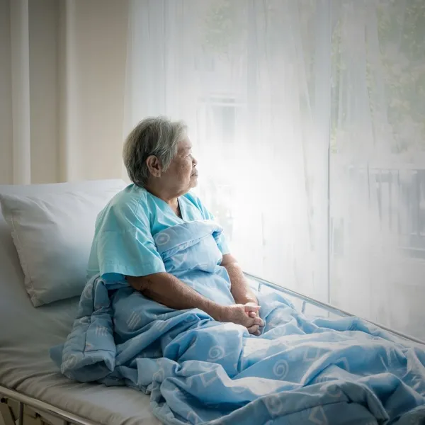 An older woman sitting up in a hospital bed beside a window